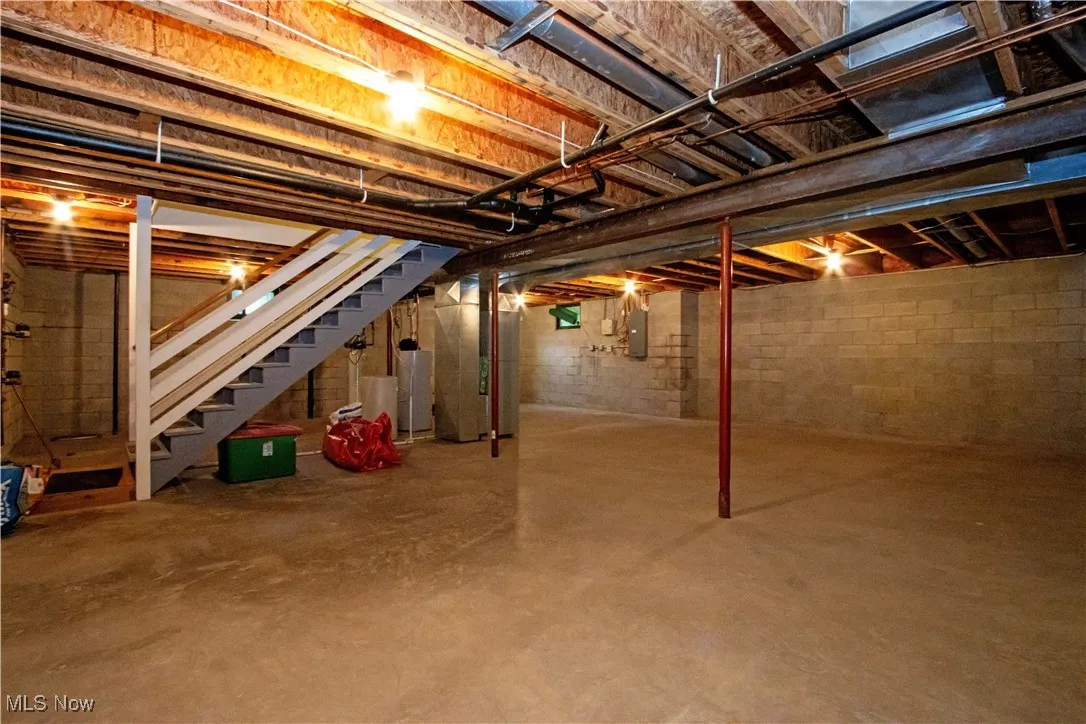 Unfinished below grade area featuring heating unit, stairway, electric panel, and water heater