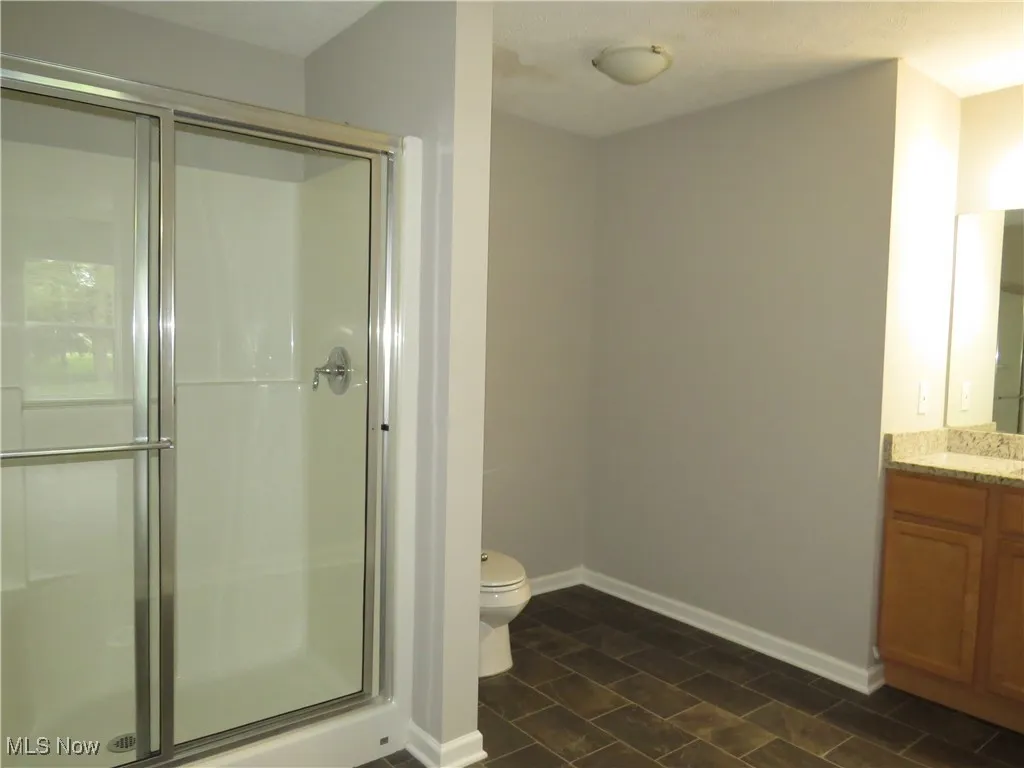 Bathroom with vanity, toilet, baseboards, and a stall shower