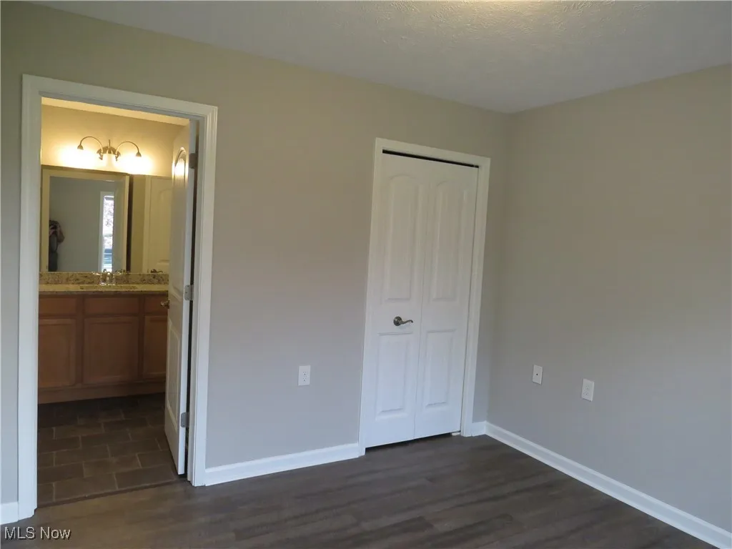 Unfurnished bedroom featuring connected bathroom, a sink, baseboards, dark wood-type flooring, and a closet