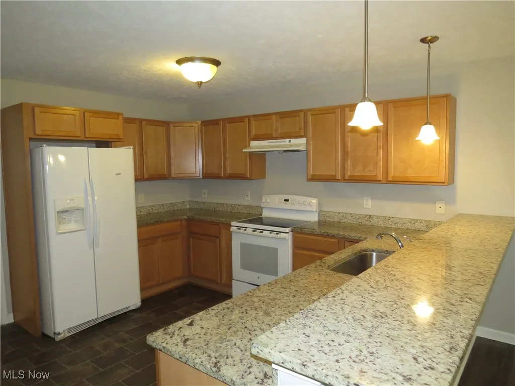 Kitchen featuring hanging light fixtures, a sink, a peninsula, under cabinet range hood, and white appliances