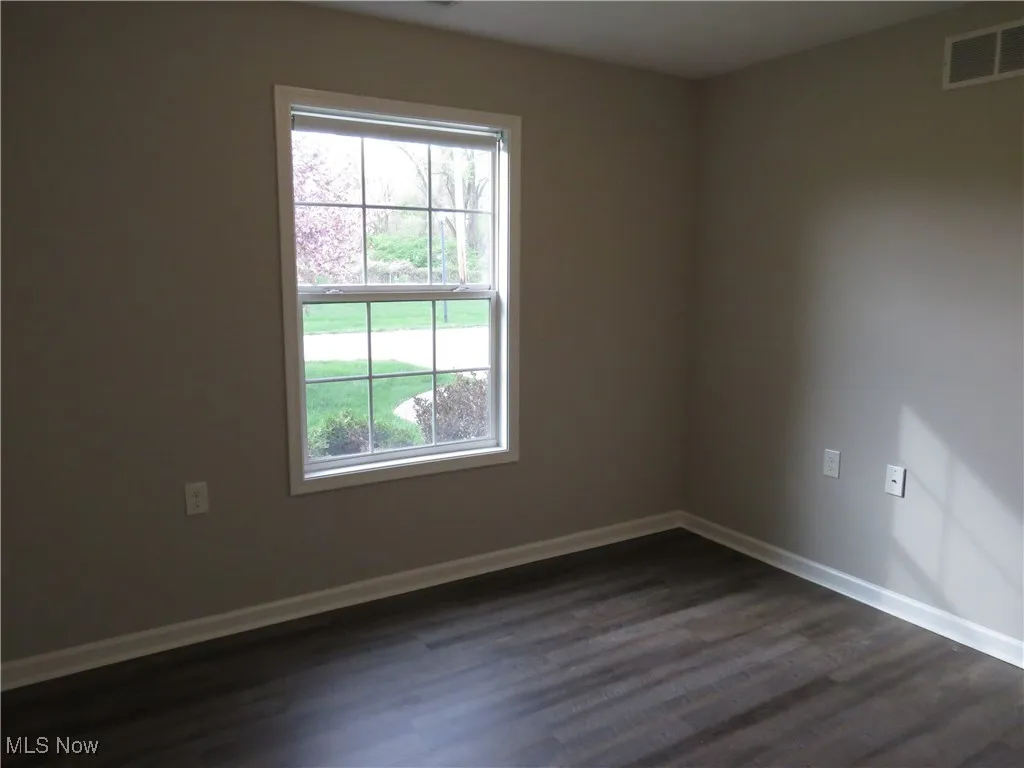 Spare room featuring visible vents, baseboards, and dark wood-style floors