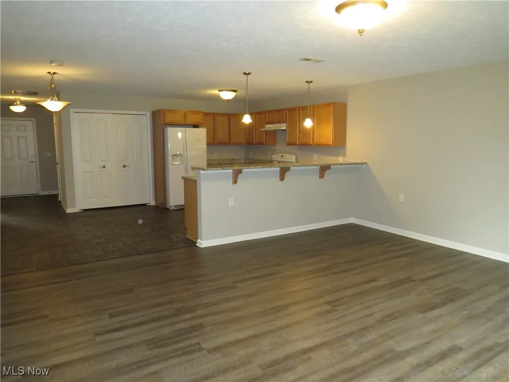 Kitchen with a kitchen breakfast bar, brown cabinetry, white refrigerator with ice dispenser, baseboards, and a peninsula