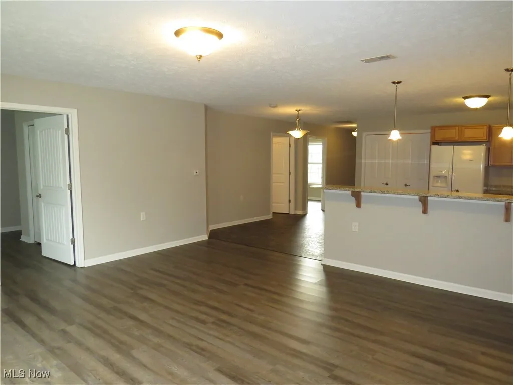 Unfurnished living room featuring baseboards, dark wood-style floors, and a textured ceiling