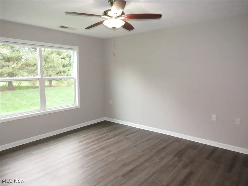 Empty room featuring visible vents, dark wood-style flooring, ceiling fan, and baseboards