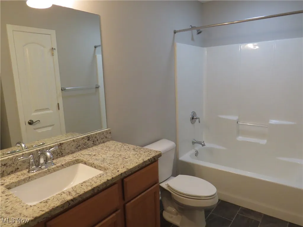 Bathroom with toilet, tile patterned floors, washtub / shower combination, and vanity