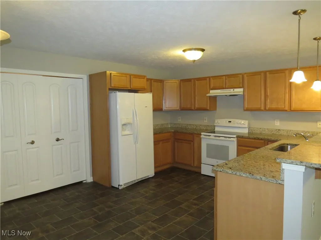 Kitchen with pendant lighting, a sink, light stone counters, under cabinet range hood, and white appliances