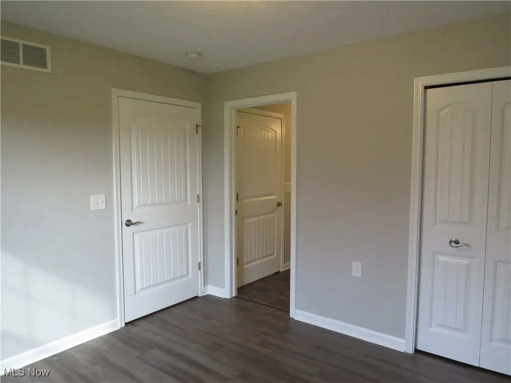 Unfurnished bedroom featuring baseboards, a closet, dark wood finished floors, and visible vents