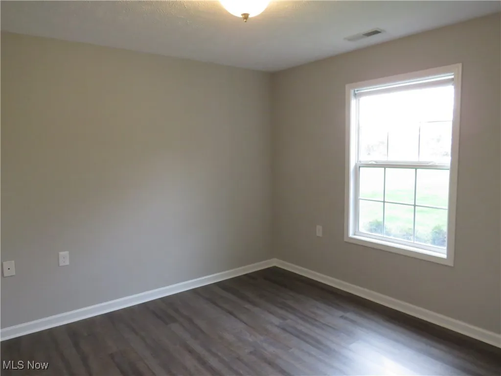 Spare room featuring visible vents, dark wood finished floors, baseboards, and a wealth of natural light