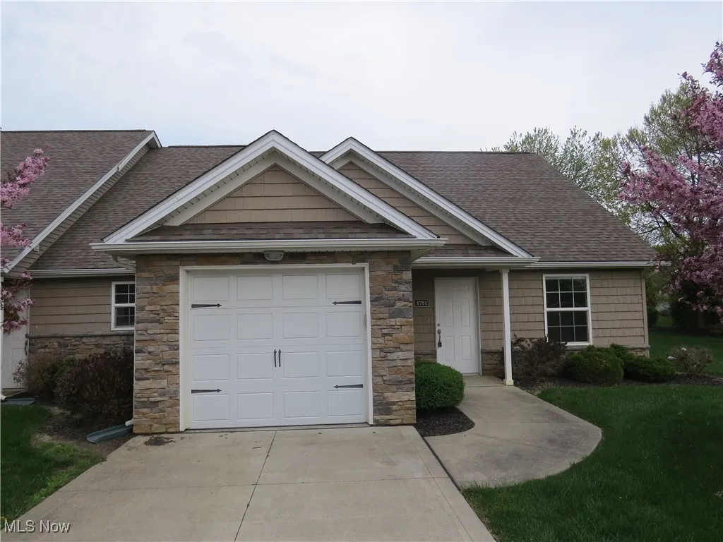 View of front of home with a garage, a front lawn, stone siding, roof with shingles, and driveway