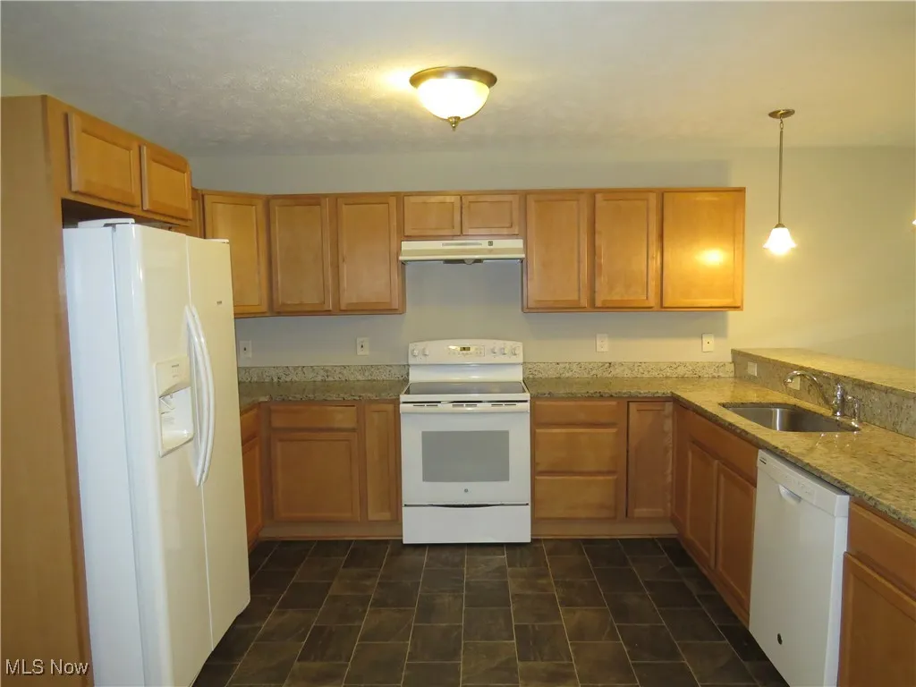 Kitchen featuring hanging light fixtures, a sink, white appliances, brown cabinetry, and under cabinet range hood