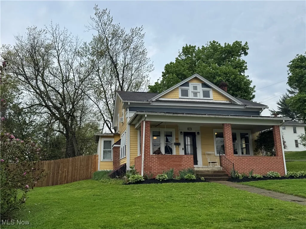 Bungalow-style home featuring covered porch, brick siding, fence, and a front yard