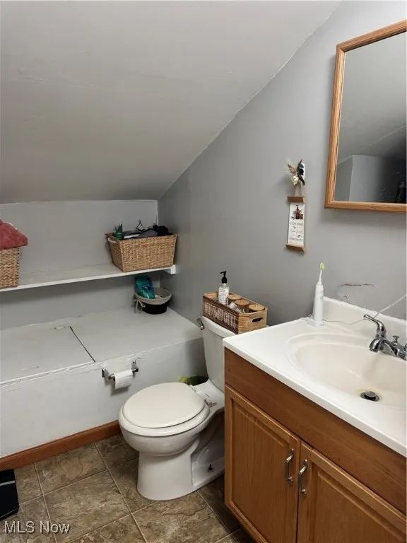Half bath with toilet, lofted ceiling, and vanity