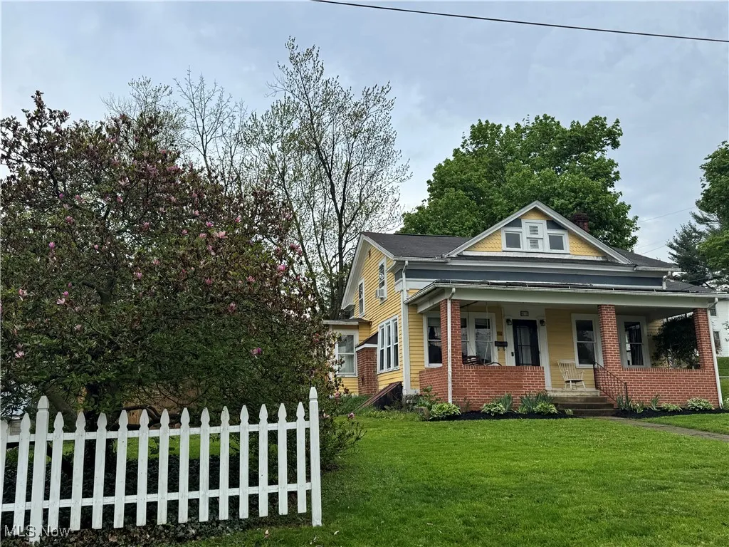 Bungalow-style home featuring fence, covered porch, a front lawn, and brick siding