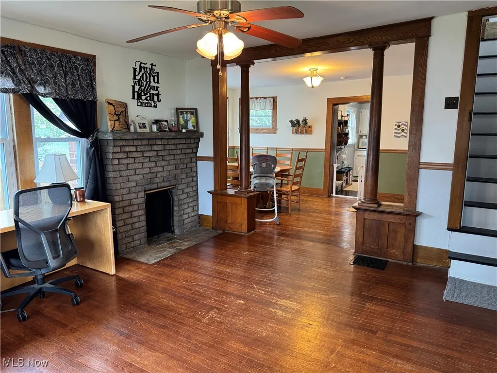 Living area with visible vents, decorative columns, a brick fireplace, wood finished floors, and a ceiling fan