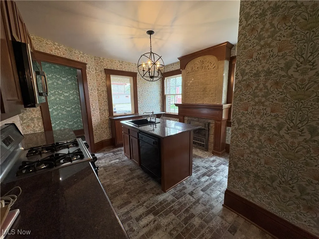 Kitchen with dishwasher, a chandelier, brick patterned floor, wallpapered walls, and baseboards