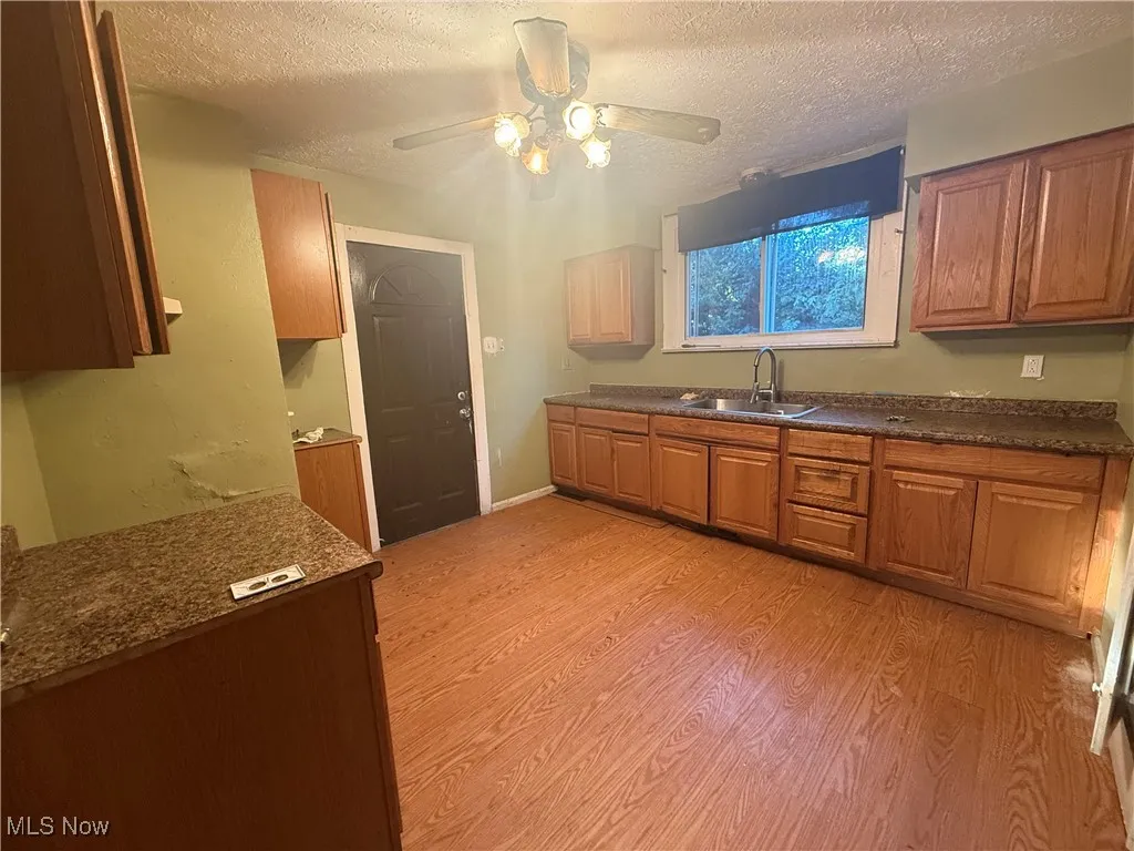 Kitchen featuring a textured ceiling, light wood-style flooring, brown cabinetry, a ceiling fan, and dark stone countertops