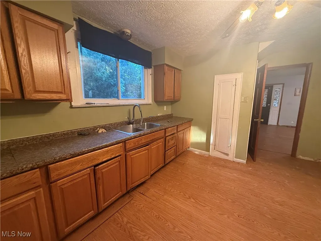 Kitchen with dark countertops, brown cabinetry, light wood-type flooring, and a textured ceiling