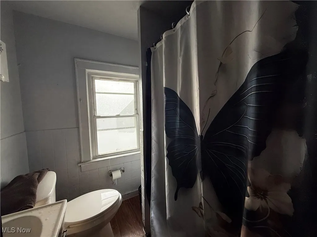 Bathroom with a wainscoted wall, wood finished floors, vanity, a shower with curtain, and tile walls