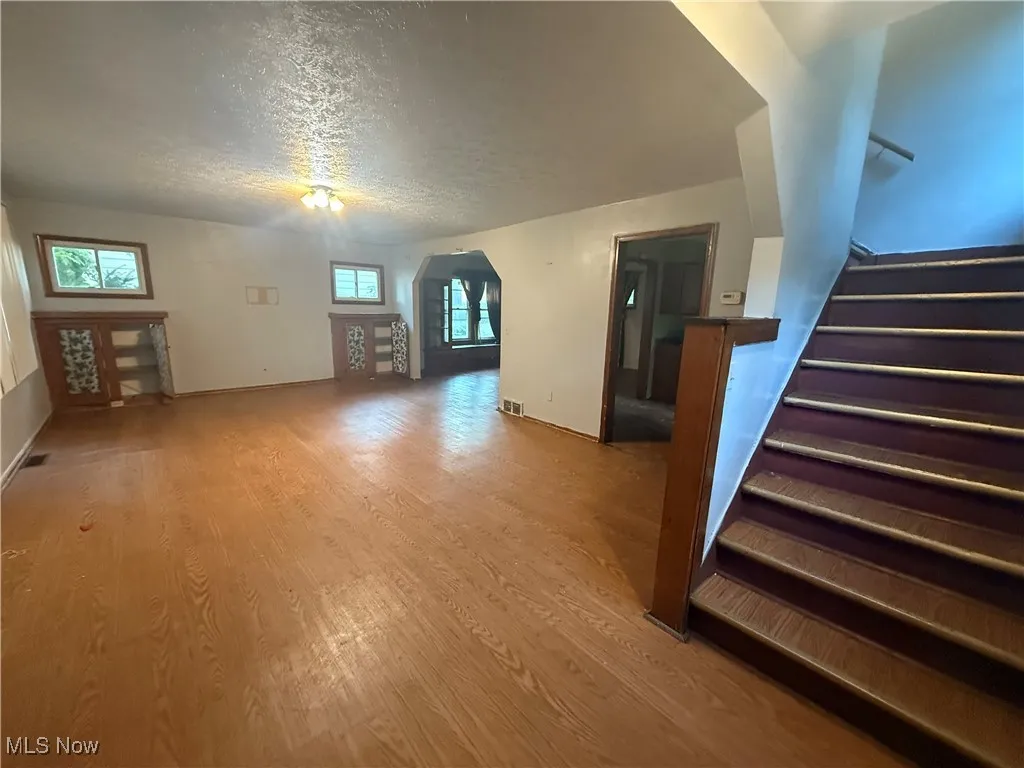 Unfurnished living room with arched walkways, wood finished floors, a textured ceiling, and stairway