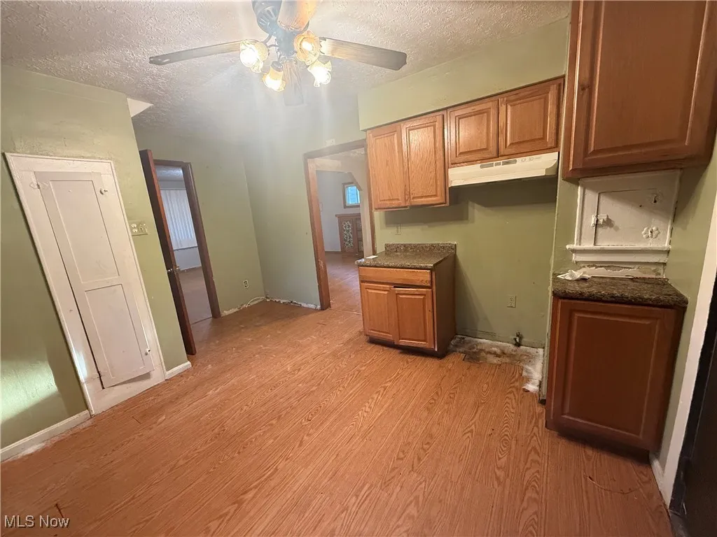 Kitchen with a textured ceiling, dark countertops, brown cabinetry, light wood-type flooring, and under cabinet range hood