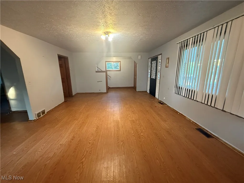 Unfurnished living room with light wood-style flooring, a textured ceiling, and arched walkways