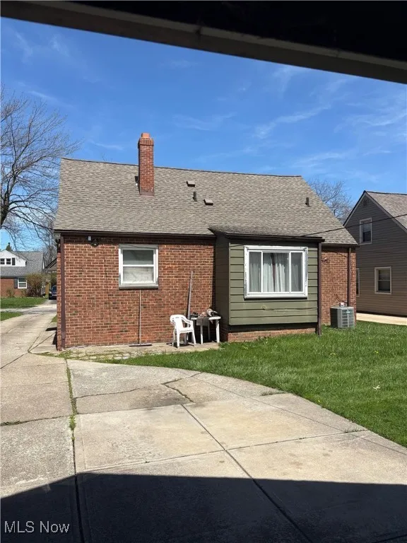 Rear view of house with brick siding, a chimney, and a shingled roof