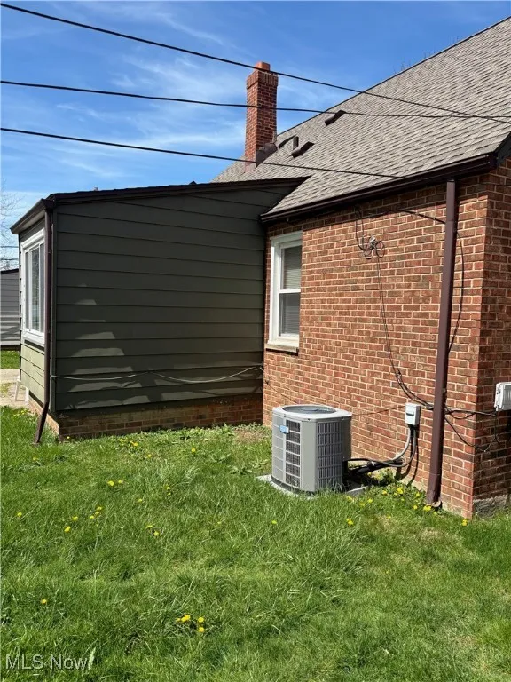 View of side of home with roof with shingles, brick siding, central AC unit, a chimney, and a yard