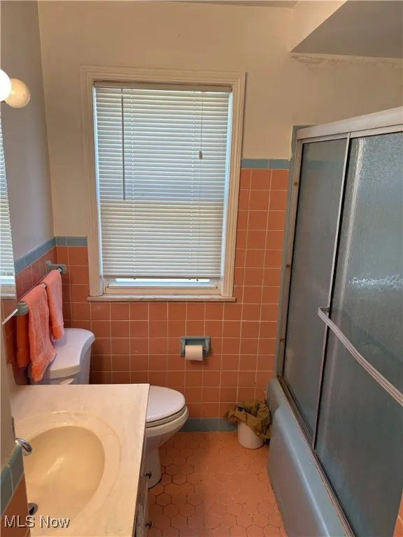Full bath featuring tile walls, tile patterned flooring, wainscoting, and toilet
