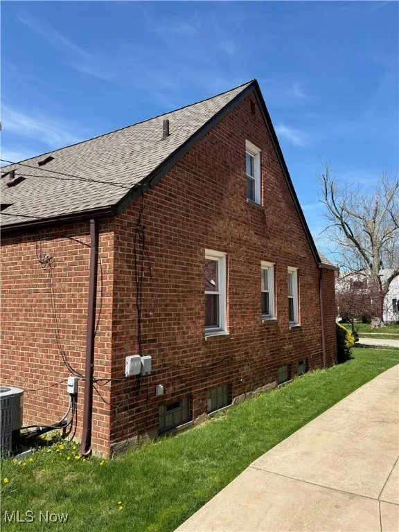 View of side of property with central air condition unit, a shingled roof, a yard, and brick siding