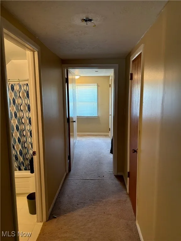 Hallway featuring a textured ceiling, baseboards, and light carpet