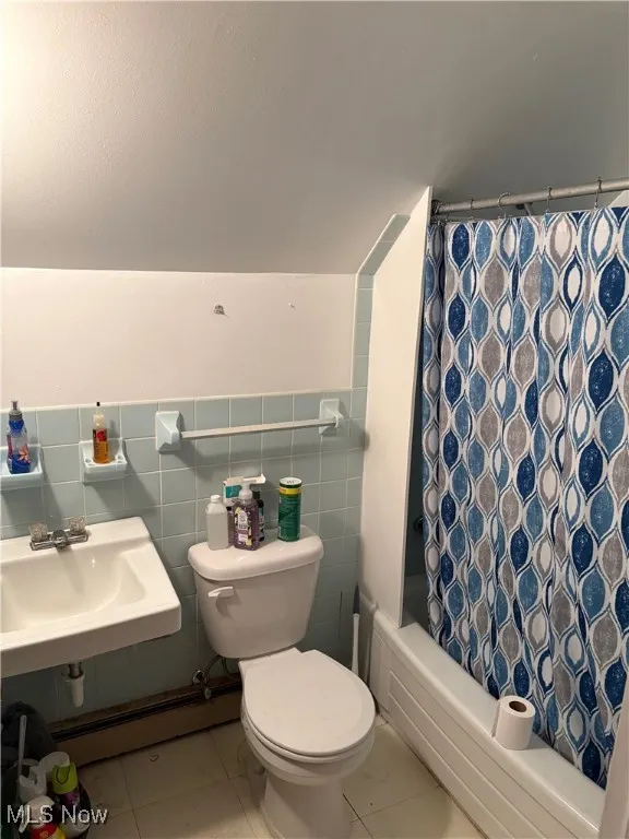Full bathroom featuring baseboard heating, a sink, toilet, tile patterned floors, and shower / bath combo with shower curtain
