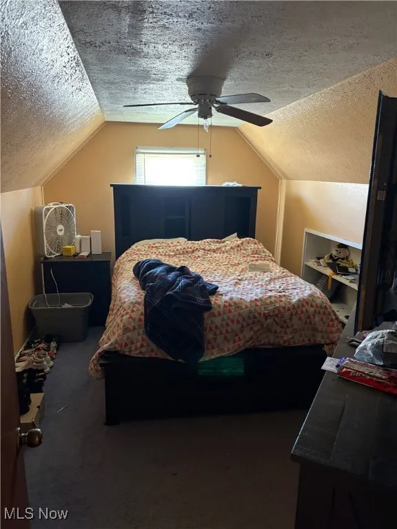 Carpeted bedroom featuring a textured ceiling, ceiling fan, and lofted ceiling