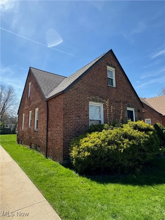 View of home's exterior featuring a yard, brick siding, and roof with shingles