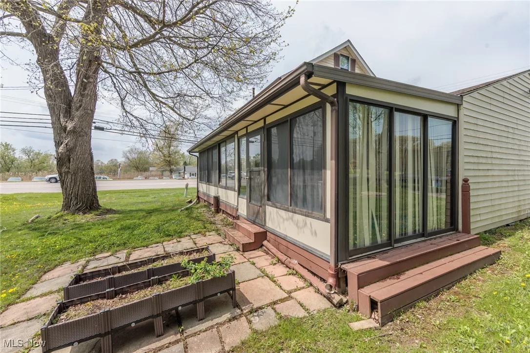 View of side of property featuring a lawn, entry steps, a garden, and a sunroom