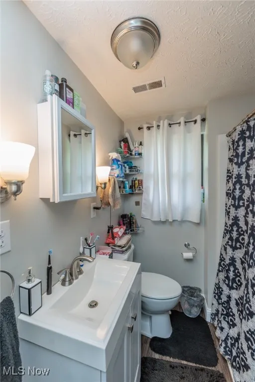 Bathroom with vanity, toilet, a textured ceiling, a shower with curtain, and visible vents
