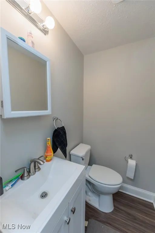 Half bath with vanity, toilet, a textured ceiling, baseboards, and wood finished floors