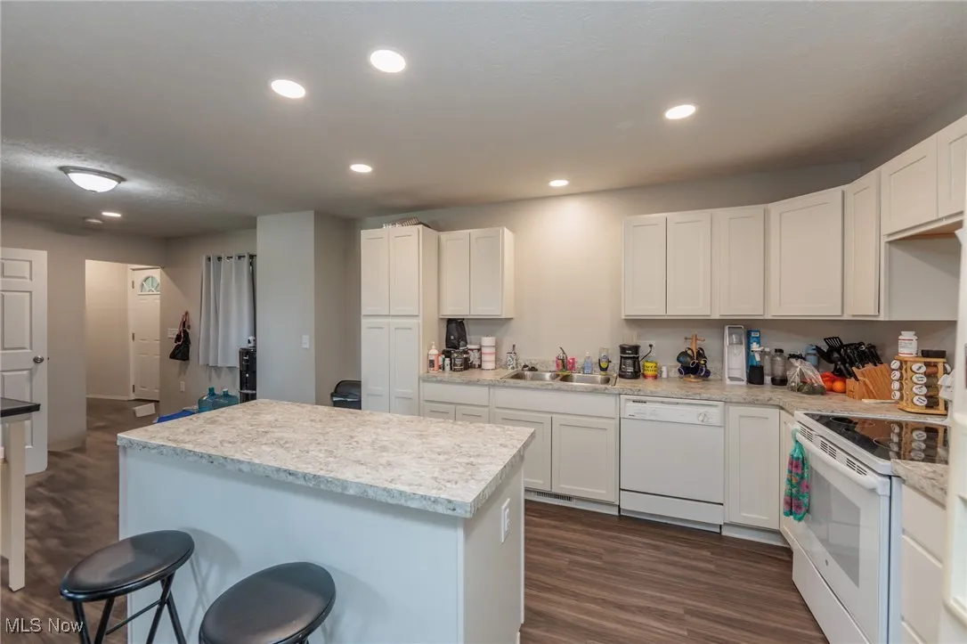 Kitchen with white appliances, dark wood-type flooring, recessed lighting, white cabinets, and a sink