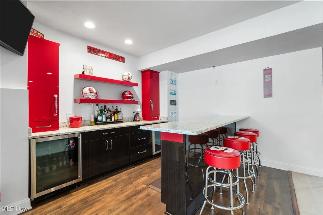 Bar with wine cooler, wood finished floors, baseboards, recessed lighting, and a dry bar