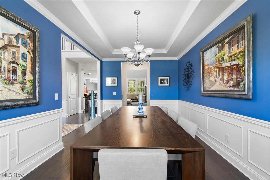 Dining room with a wainscoted wall, a raised ceiling, wood finished floors, and a notable chandelier