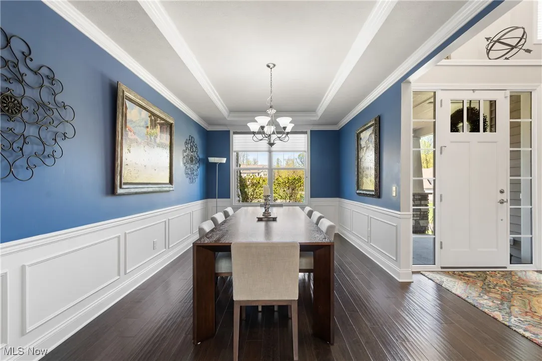 Dining area featuring dark wood-style flooring, a decorative wall, a chandelier, a wainscoted wall, and a tray ceiling