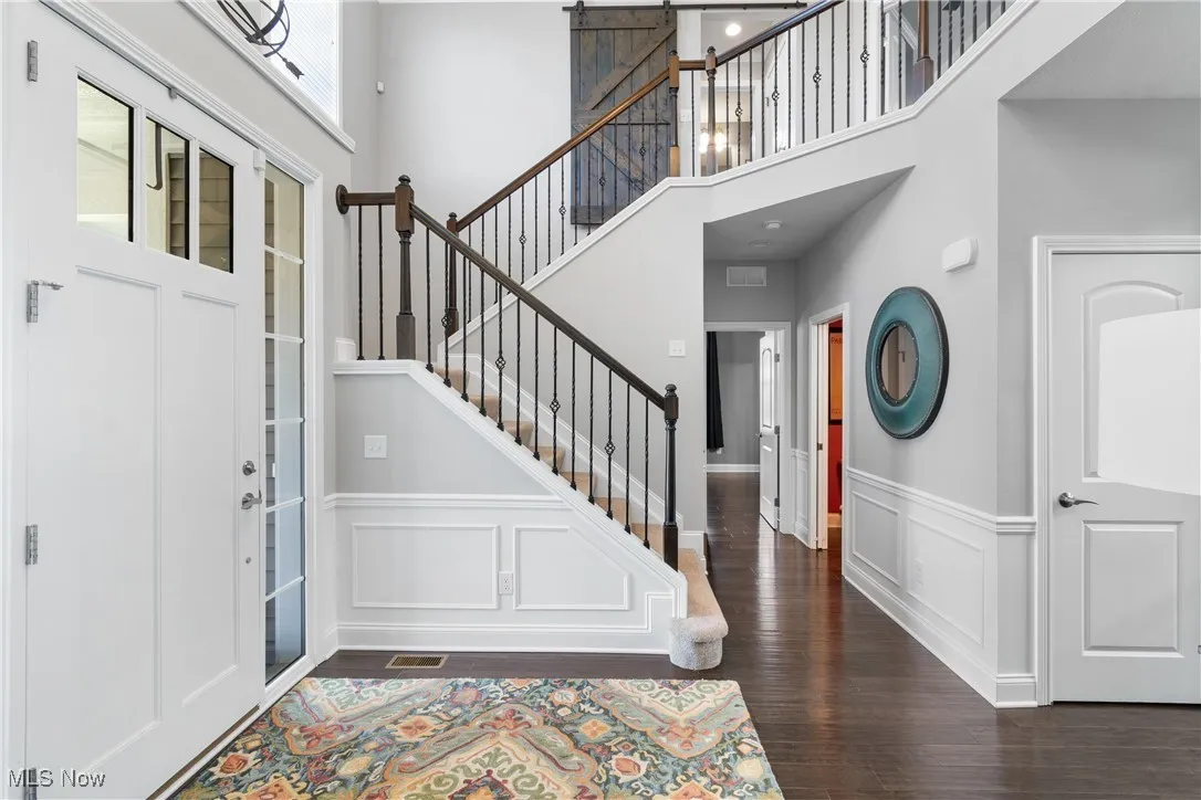 Foyer featuring a high ceiling, wainscoting, a decorative wall, wood finished floors, and stairway
