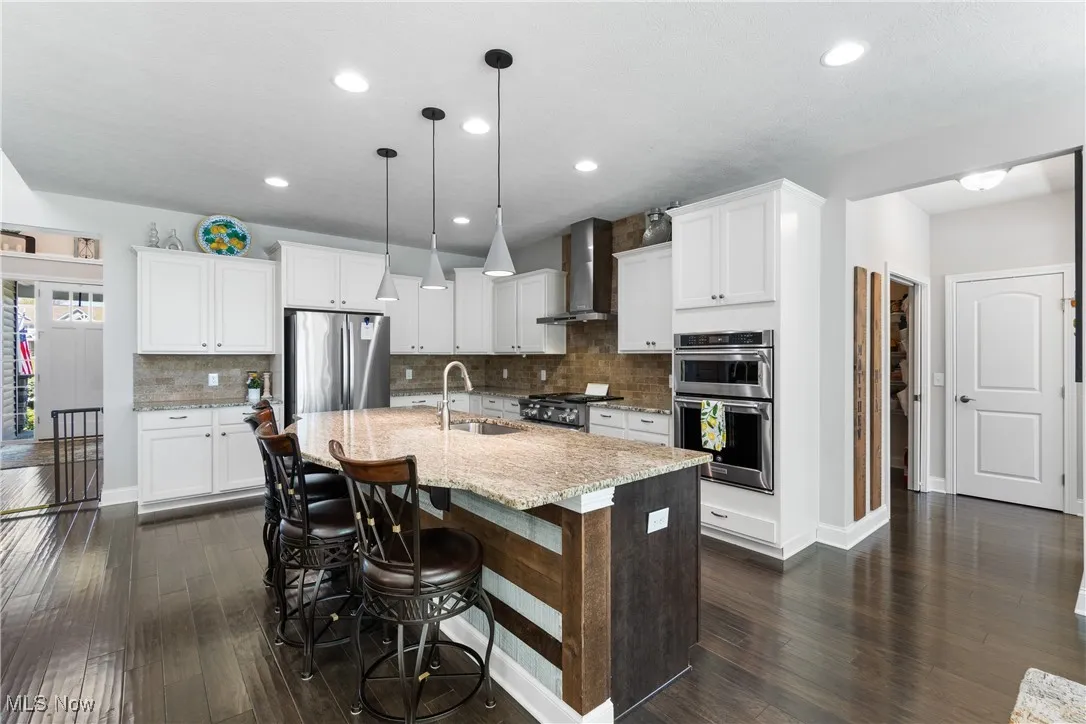 Kitchen with decorative backsplash, dark wood-style floors, wall chimney range hood, a sink, and stainless steel appliances
