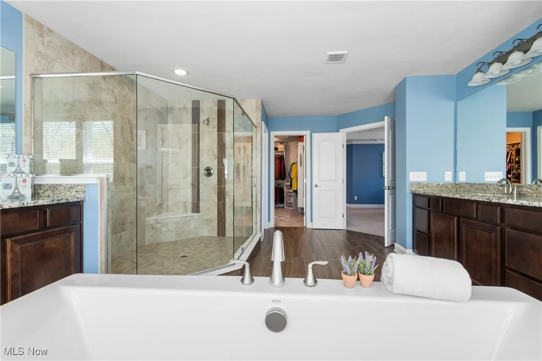 Full bath with vanity, visible vents, wood finished floors, a walk in closet, and a shower stall