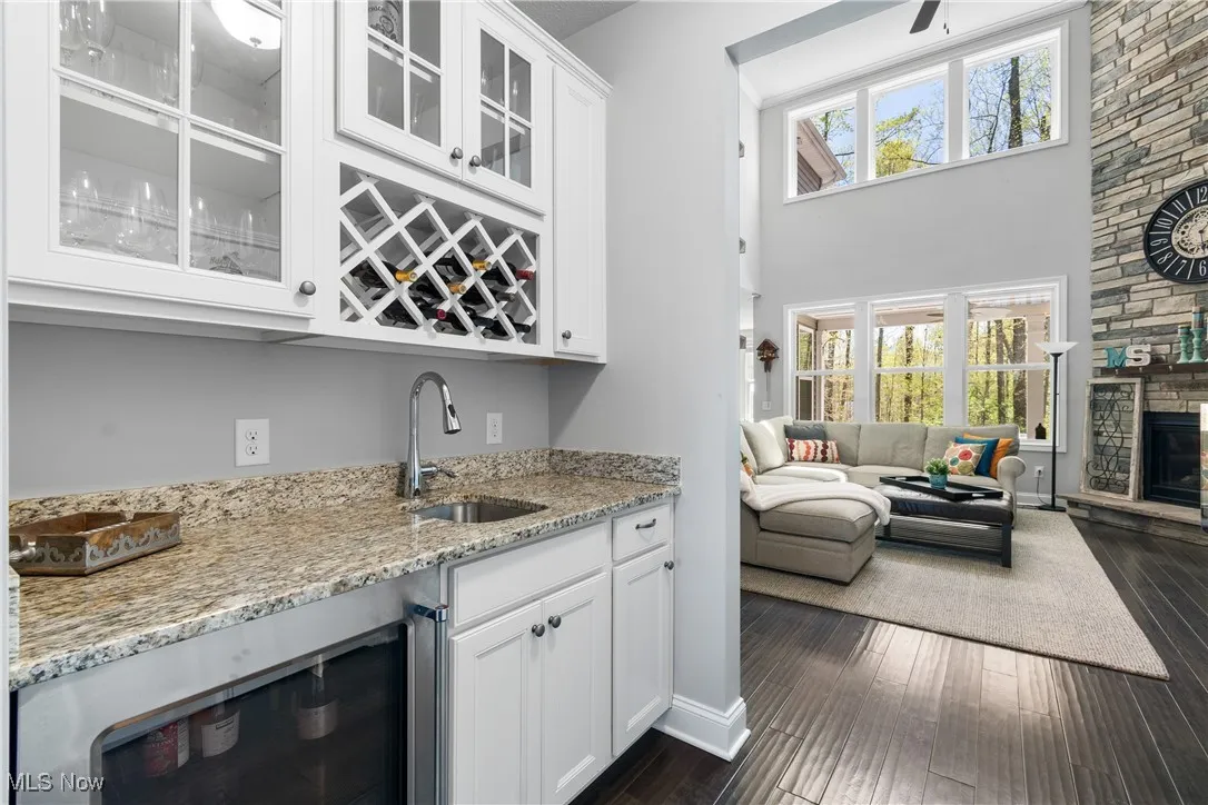 Bar featuring a sink, beverage cooler, a stone fireplace, indoor wet bar, and dark wood-style floors