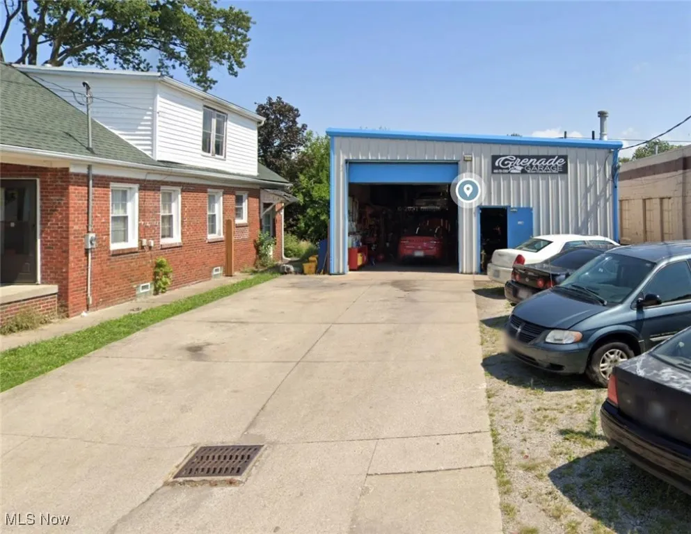 View of property exterior with brick siding, an outdoor structure, roof with shingles, and driveway
