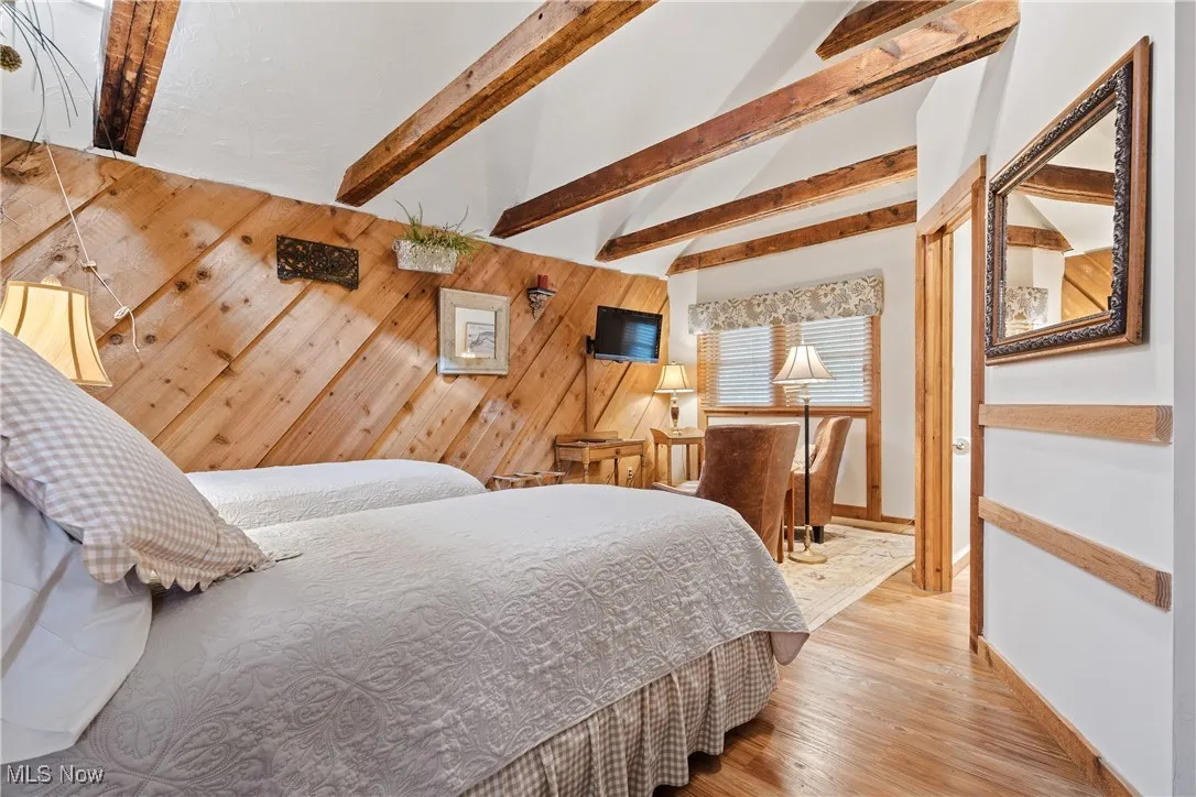Bedroom with vaulted ceiling with beams, baseboards, wood finished floors, and wooden walls