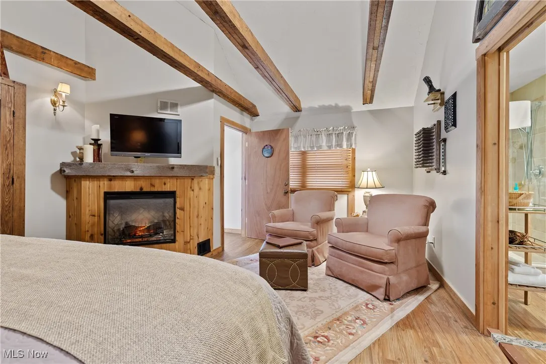 Bedroom featuring visible vents, beam ceiling, wood finished floors, baseboards, and a glass covered fireplace