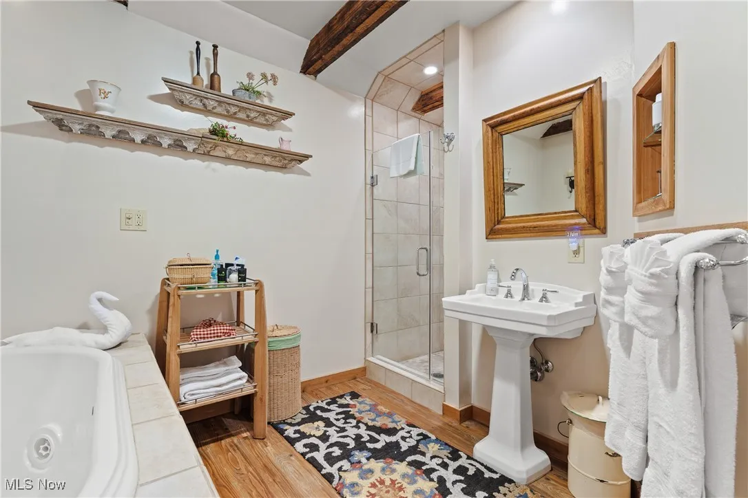 Full bath with wood finished floors, beamed ceiling, baseboards, a jetted tub, and a stall shower