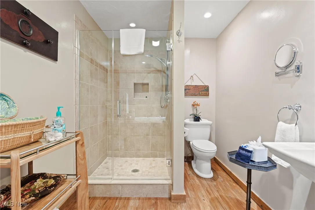 Bathroom with a stall shower, wood finished floors, baseboards, toilet, and recessed lighting