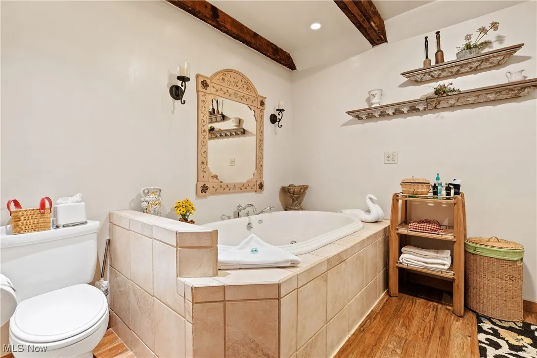 Bathroom featuring a jetted tub, beamed ceiling, toilet, and wood finished floors